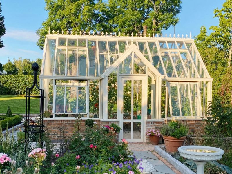 Oranjerie victoriană Floribunda cu verandă frontală și soclu din cărămidă, într-o grădină înflorită