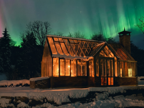 Oranjerie Multiflora iarna, cu ferestrele luminate și auroră boreală deasupra